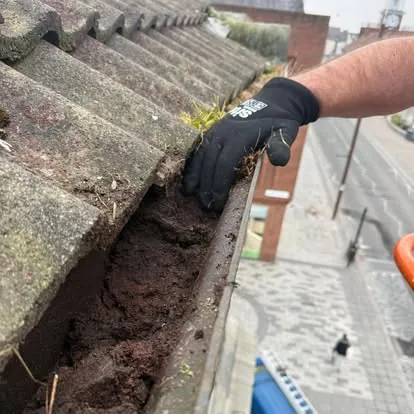 Vegetation being removed by hand from a blocked masonry gutter
