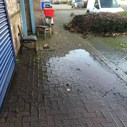 Commercial block-paved passage before cleaning, algae-darkened paving between brick walls